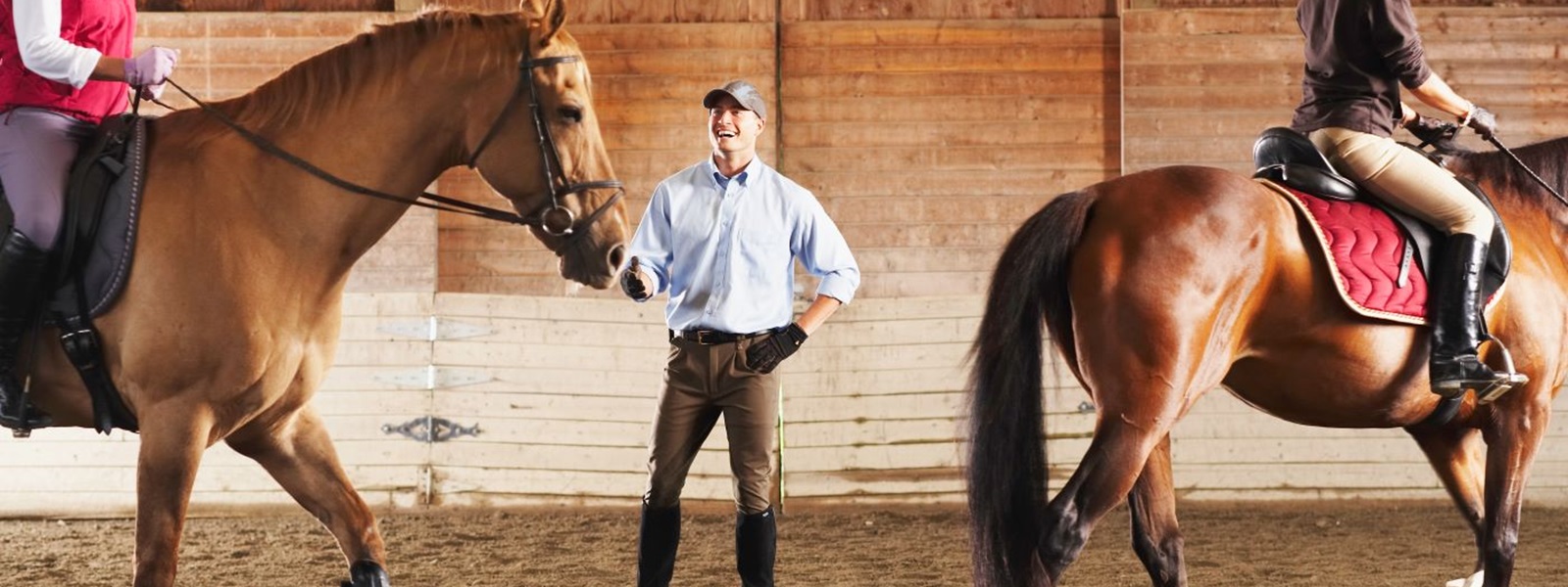 Trainer encourages two students on horseback in a barn